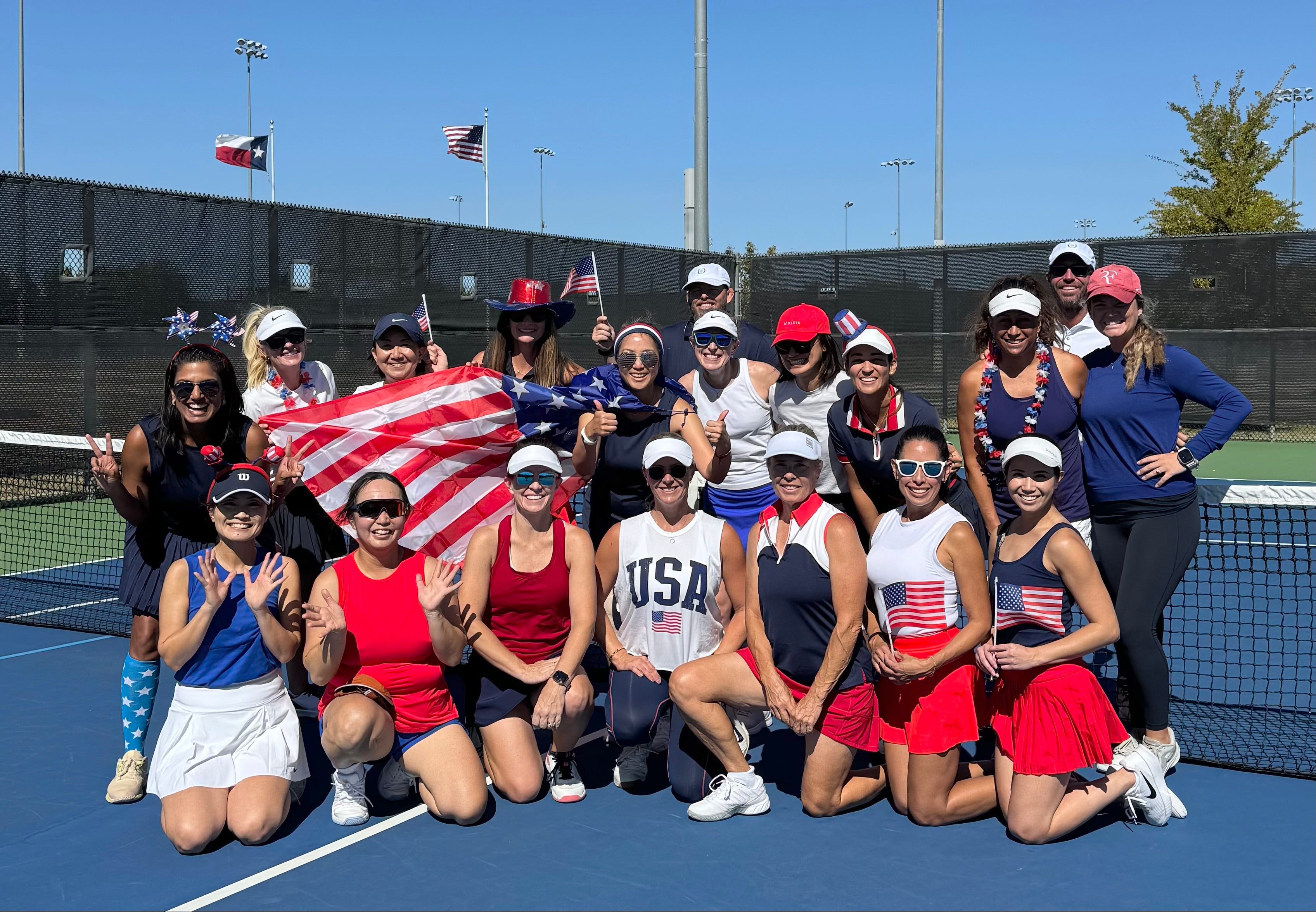 Group of tennis players posing on a tennis court with a clear blue sky.