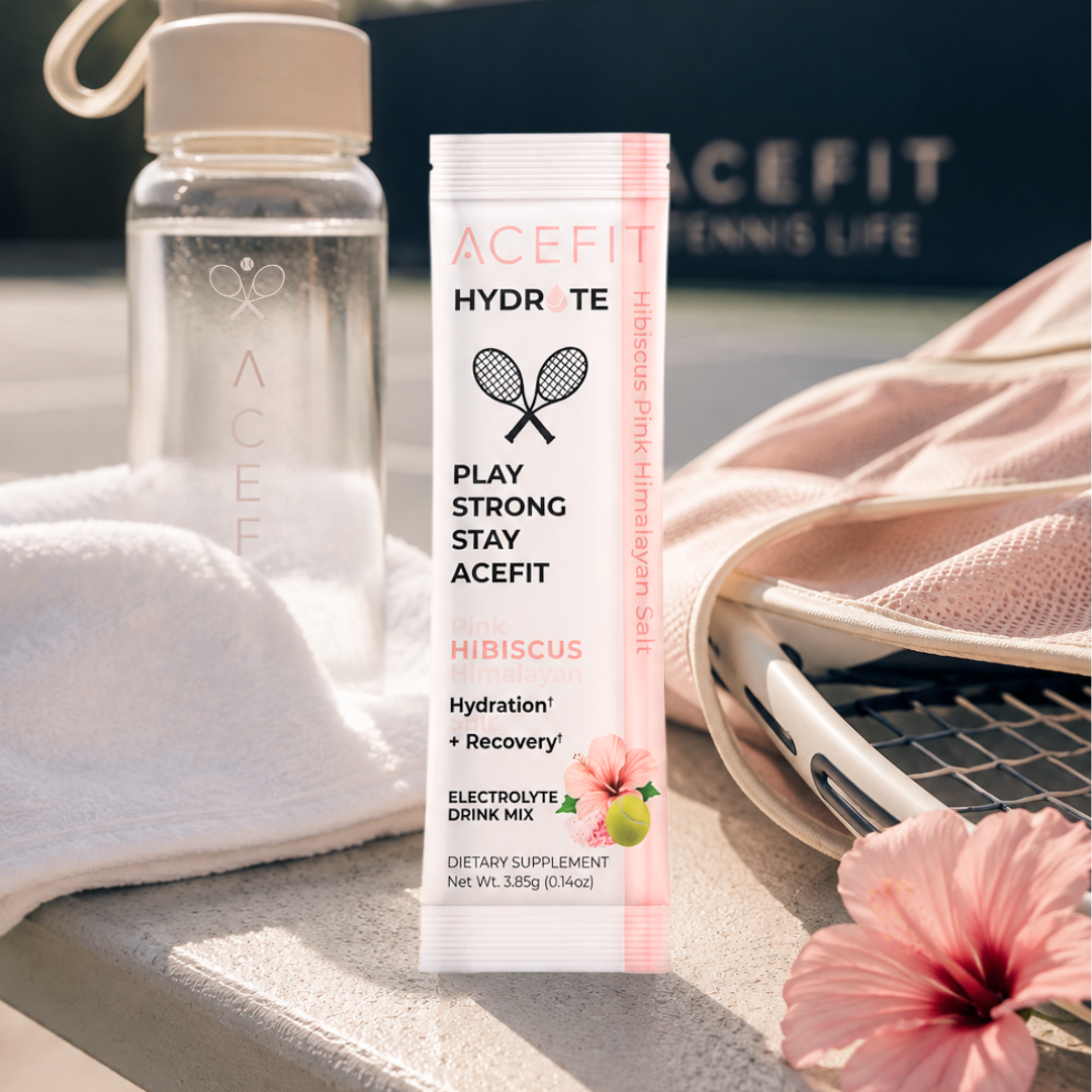 ACEFIT Hydrate electrolyte drink mix packet on a tennis court table next to a clear water bottle, pink towel, tennis bag, and hibiscus flower.